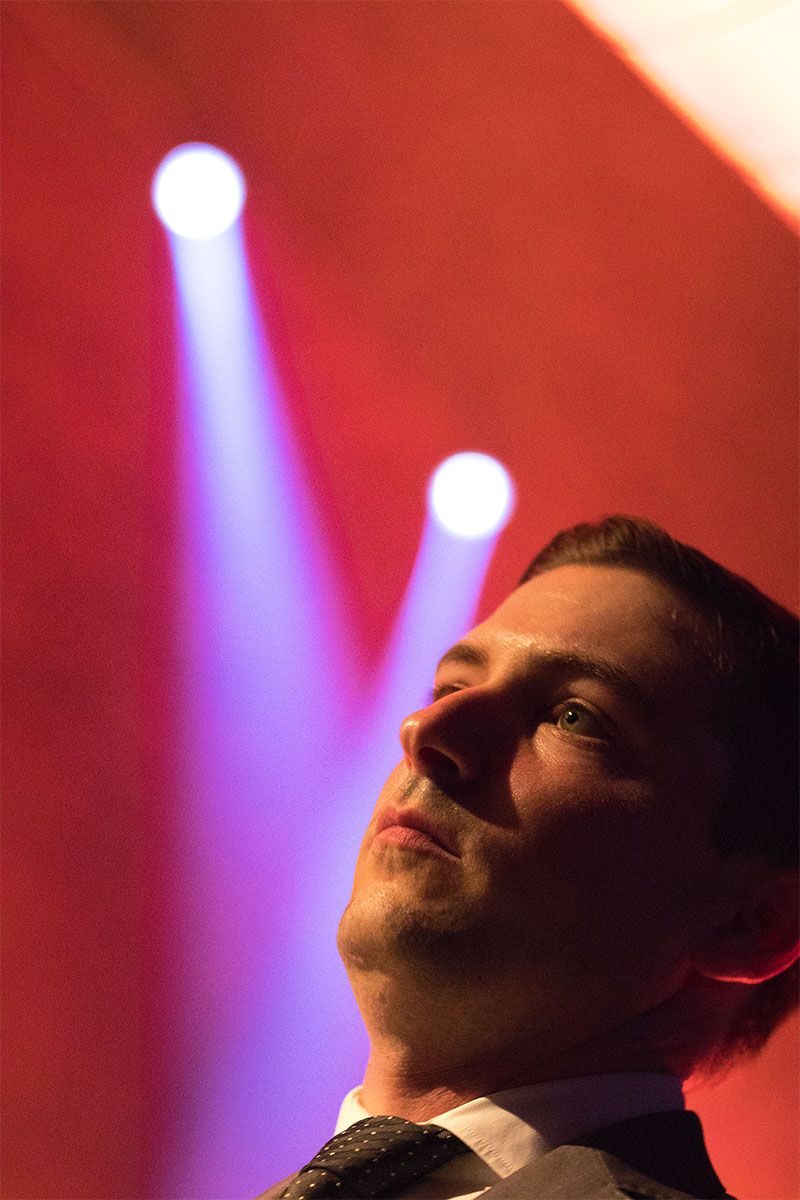 A business man in a suit on stage, staring into the distance.