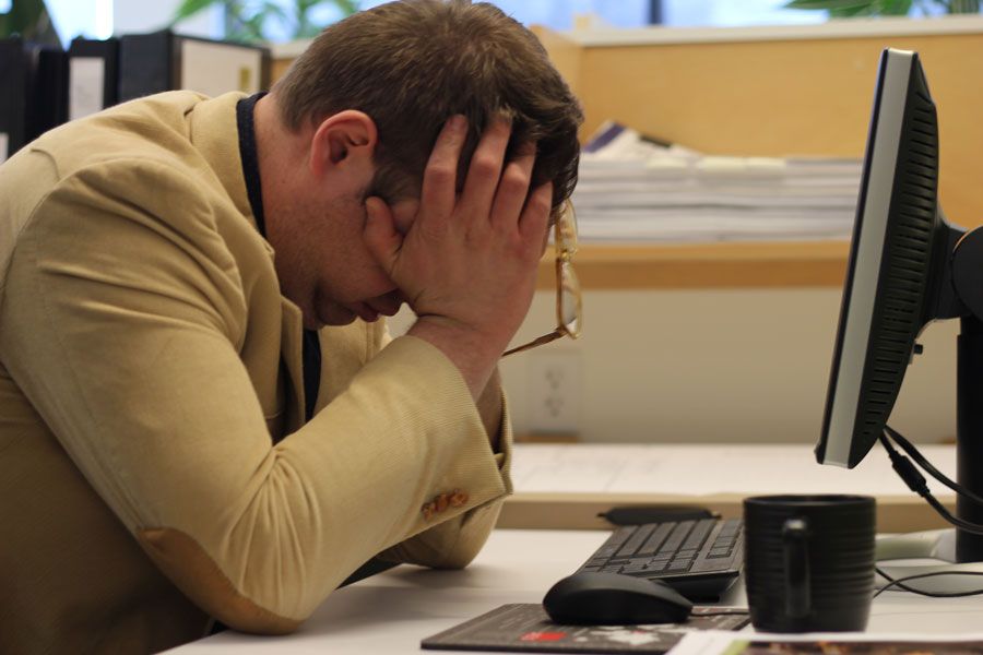 A businessman holding his head in his hands while working on a laptop.