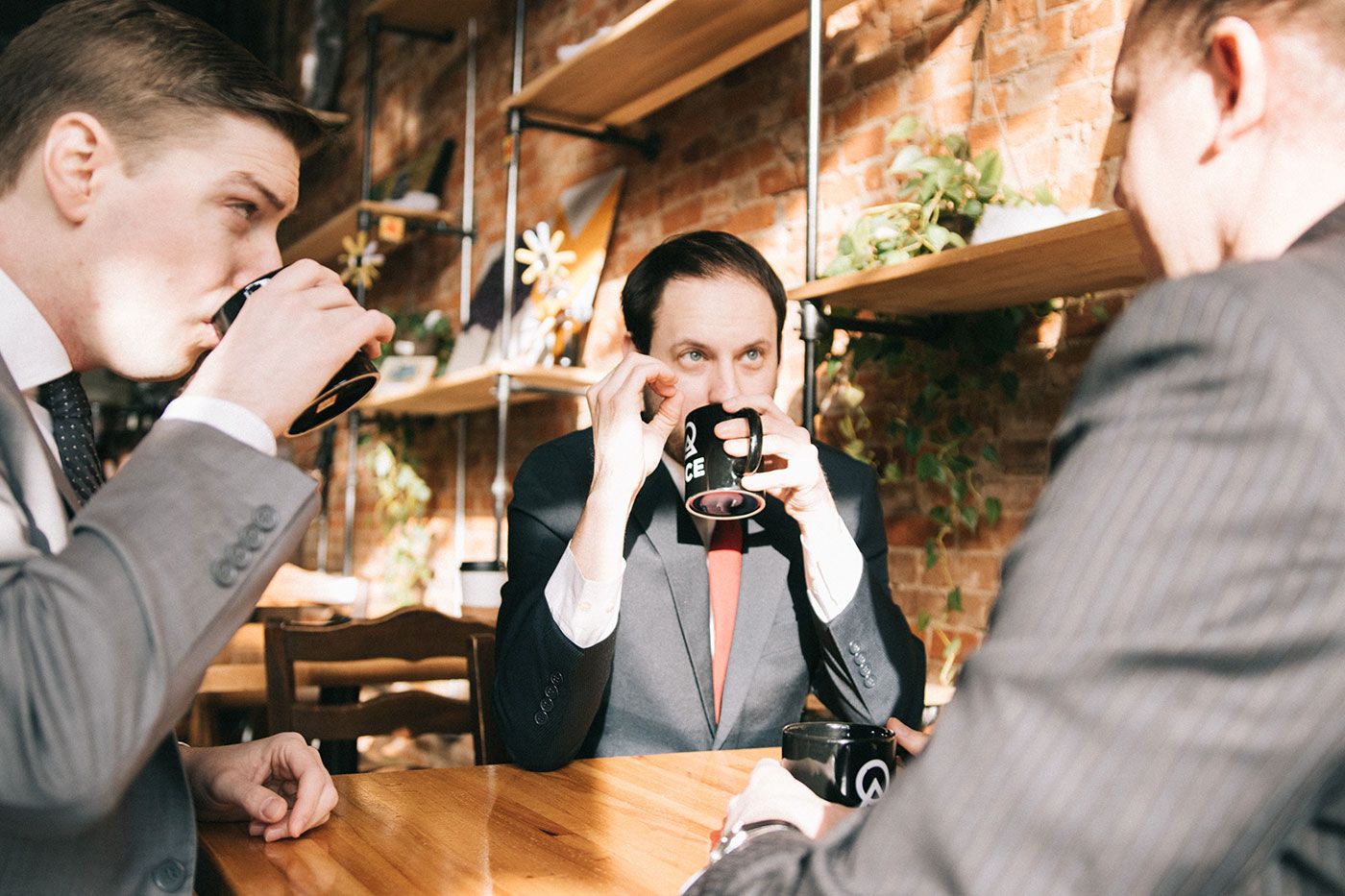 Three businessmen laughing in front of a crane. One has their hand raised in a fist.