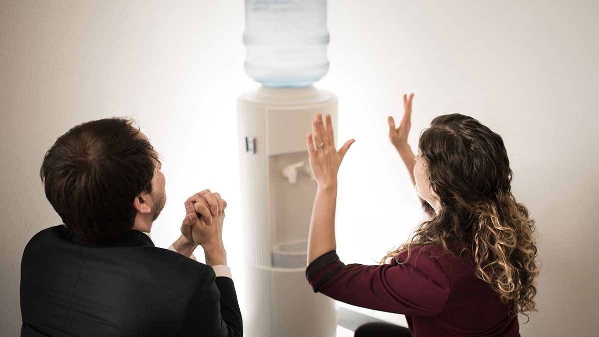 Two RCE employees at a water cooler, hands held high and in prayer as an act of worship.